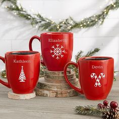 three red coffee mugs sitting on top of a wooden table next to christmas decorations