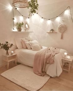 a bedroom with white walls and wooden flooring, lights strung from the ceiling over the bed