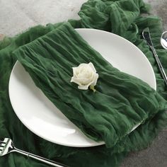 a white rose sitting on top of a green napkin next to a fork and knife