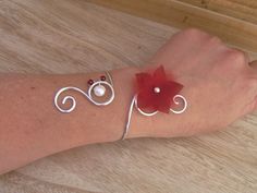 a woman's arm with two bracelets and a red flower on the wrist