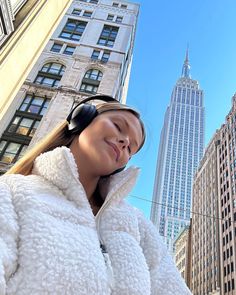 a woman wearing headphones standing in front of tall buildings with the empire building in the background