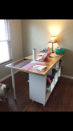 a dog is standing in front of a desk with books and papers on it, next to a lamp