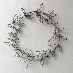 a wire wreath with leaves is shown against a white background, it looks like an artistic piece of art