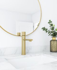 a bathroom sink with a gold faucet next to a round mirror on the wall