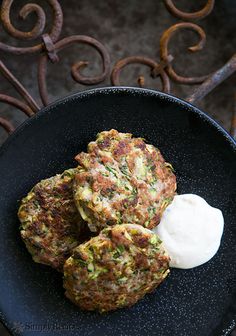 three crab cakes on a black plate with sour cream