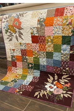 a large quilt is on the floor in front of a table with a vase and flowers