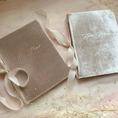 two wedding books with ribbons on them sitting next to each other in front of some dried grass