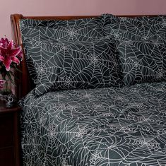 a bed with black and white comforter next to a night stand on a wooden table