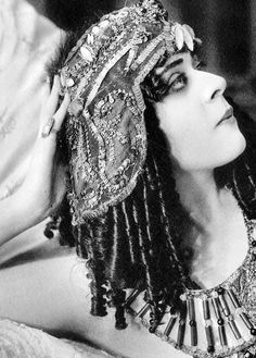 an old photo of a woman wearing a headdress and holding her hair up to her face