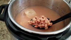 a spoon with some food in it sitting inside of a crock pot on the stove