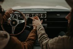 two people sitting in the driver's seat of a car with their hands on the steering wheel