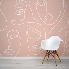 a white chair sitting in front of a pink wall with faces drawn on the wall