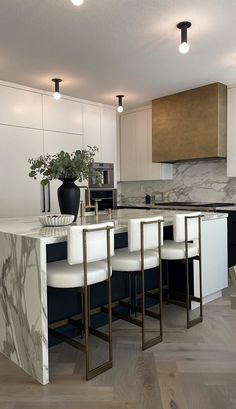 a modern kitchen with marble counter tops and white stools, along with wooden flooring