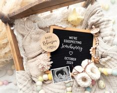 a baby announcement is displayed on a blackboard surrounded by white and pink eggs, crocheted mittens, and other decorations