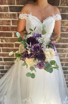 a woman wearing a wedding dress holding a bouquet of flowers in front of a brick wall