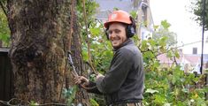 a man in an orange helmet is holding a tree branch and smiling at the camera