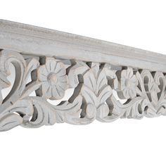 an ornately carved white wood shelf with flowers on the top and bottom, against a white background