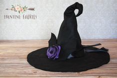 a black hat with a purple rose on it sitting on top of a wooden table