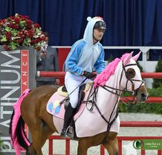 a man riding on the back of a brown horse next to a red fence and flowers