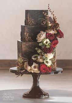 a three tiered cake decorated with flowers and leaves on a metal stand in front of a wall