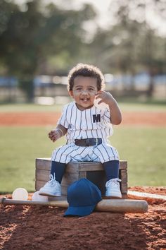 a little boy sitting on top of a wooden box in a baseball field wearing a hat