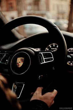 the steering wheel of a porsche car is seen in this image, while someone's hands are on the dashboard