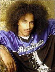 a man with an afro sitting on the ground wearing a purple shirt and chain around his neck