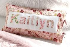 a pink pillow with the word kalli on it next to a white fluffy animal