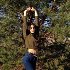 a woman is standing in front of some trees and holding her hands above her head