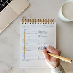 a person holding a pencil next to a notebook with a list on it and a laptop in the background