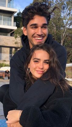 a man holding a woman in his arms while she smiles at the camera with her arm around him