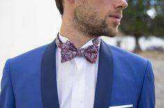 a man wearing a blue suit with a red flowered bow tie and white shirt