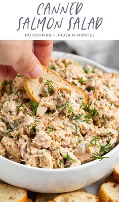 a hand dipping a piece of bread into a bowl of salmon salad with dill sprigs