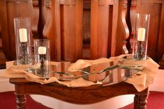 a wooden table topped with two glass vases next to candles on top of it