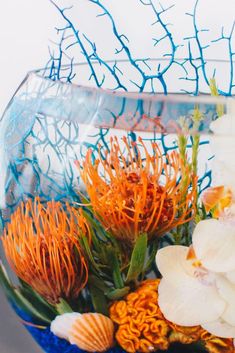 an arrangement of flowers and seashells in a glass bowl