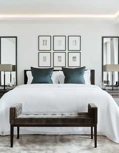 a white bed with blue pillows and pictures on the wall above it in a bedroom