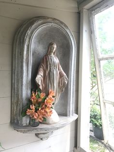 a statue on the wall with flowers in front of it