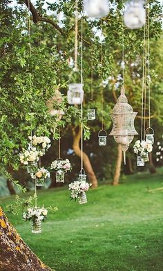 an outdoor wedding ceremony with hanging lanterns and floral centerpieces on the tree branch