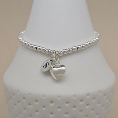 This gorgeous personalised silver-plated bead bracelet has a stunning polished silver heart charm. Personalise the bracelet with solid silver letter charms. The bracelet is available in a standard 16cm size or larger 19cm size. Threaded onto strong jewellery elastic. If you would like two or three letter charms adding to your bracelet, please select the relevant option from the 'Letter Charm' option box. Please then let us know, in the personalisation box, which letters you would like. Our free Sterling Silver Charm Bracelet With Initials In Silver, Silver Charm Bracelet With Letter Beads As Gift, Silver Charm Bracelet With Letter Beads For Gift, Silver Dainty Charm Bracelet With Heart Beads, Personalized Silver Heart Bracelet With Charms, Dainty Silver Charm Bracelet With Heart Beads, Silver Heart-shaped Dainty Beaded Bracelets, Dainty Silver Beaded Bracelets With Heart Charm, Personalized White Gold Heart Charm Bracelet