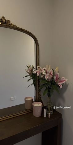 a vase filled with flowers sitting on top of a wooden table next to a mirror