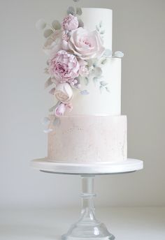 a three tiered white cake with pink flowers on top and silver leaves around the edges