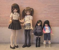 three dolls standing next to each other in front of a brick wall with their hands together