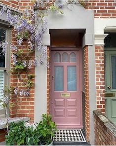 a pink front door on a brick building with potted plants in the foreground