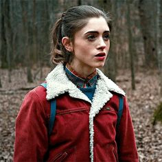 a woman in a red jacket is standing in the woods