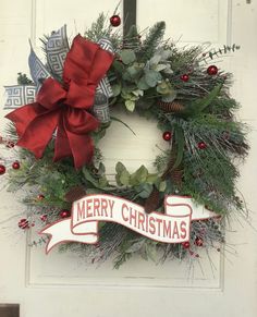 a christmas wreath hanging on a door with a merry christmas ribbon around the wreath and bow