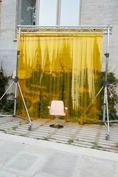 a chair sitting in front of a yellow curtain on the side of a building next to a window