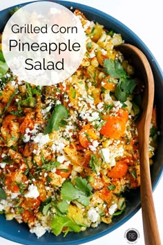 a blue bowl filled with fried corn, pineapple and carrot salad next to a wooden spoon