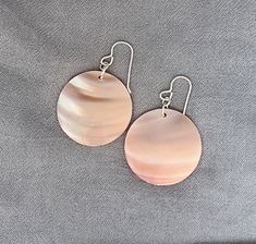 This delicate mother of pearl shell is really pretty. Each shell is unique with its own lovely iridescent shimmer. These simple statement earrings are 30MM round discs and hang from a sterling silver earring hook. The front and back of the shell has a glossy finish over natural variations.  The color of the shell is a soft peachy pink which changes slightly with lighting and natural environment. The photos of this product listing show the same pair of earrings -- just in different lighting.    Fun pink shell earrings Large pink statement earrings Unique mother of pearl earrings Lightweight natural shell Sterling silver earring wire Elegant and simple MOP earrings for pierced ears The earrings arrive with their own Greta Jones cloth storage pouch and gift box. Earring drop: 1.75 inches or a Pink Statement Earrings, Cloth Storage, Pearl Statement Earrings, Vacation Jewelry, Earring Wire, Mother Of Pearl Earrings, Earring Hook, Summer Earring, Product Listing