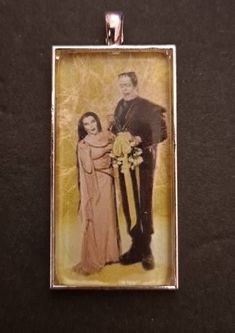 "This 1\" x 2\" rectangular pendant features one of the greatest monster love stories of Classic TV, Herman and Lily Munster. This looks as if it is a wedding or anniversary pose and the sunny yellow background is glorious!  Comes with your choice of 24\" silver chain, 30\" silver ball chain, or silver keychain." Herman And Lily Munster, Lily Munster, Silver Keychain, Photo Pendant, Sunny Yellow, The Shining, Love Stories, Yellow Background, Classic Tv