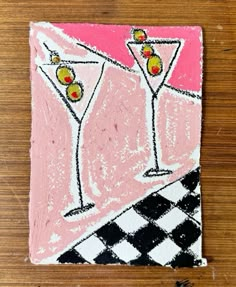 a pink and black tile with two martini glasses on it's side, sitting on a wooden surface